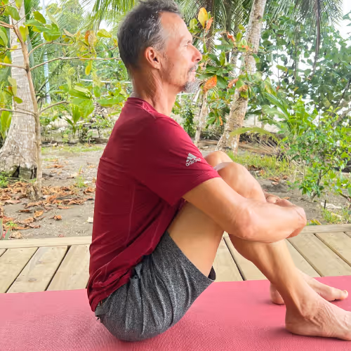Mann sitzt auf Yogamatte im Schneidersitz und meditiert im Freien unter Bäumen.