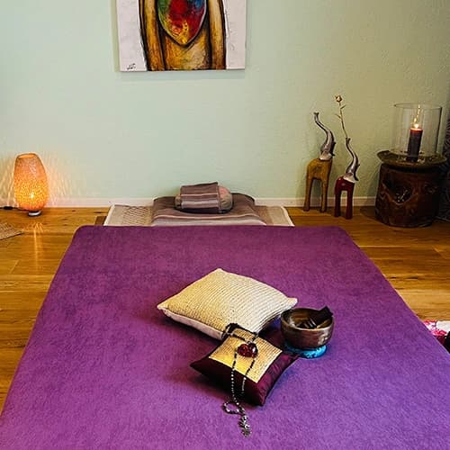 Violette Massagematte mit Kissen, Kerze und Laterne im warm beleuchteten Praxisraum