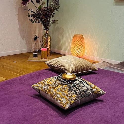 Massagebereich der Praxis mit violetter Matte, goldenen Kissen und warmem Lampenlicht