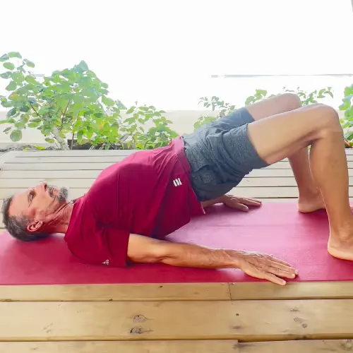 Mann macht eine Brücke-Übung auf einer Yogamatte im Freien mit Pflanzen im Hintergrund.