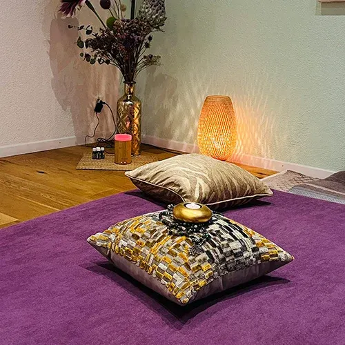 Massagebereich der Praxis mit violetter Matte, goldenen Kissen und warmem Lampenlicht