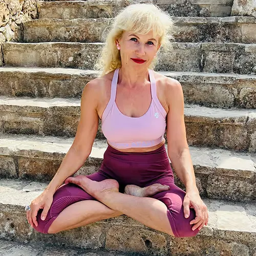Frau mit blonden Haaren in sportlichem Outfit sitzt im Lotussitz auf Stein-Treppen.
